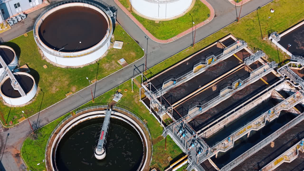 Aerial perspective of industrial water processing basins and tanks. Complex of rectangular and circular water treatment structures separated by asphalt paths and green lawns