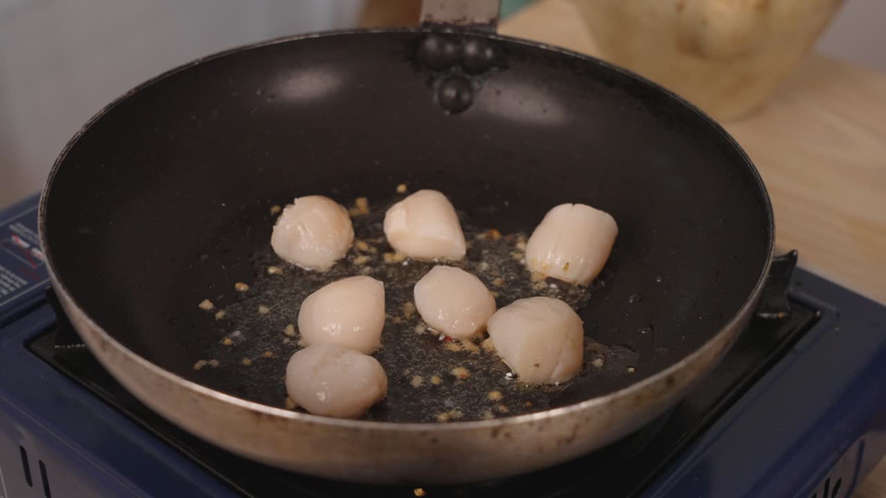 Outdoor camping concept with portable portable butane gas stove cooker cooking delicious seafood scallops, sizzling on shallow frying pan, close up static shot