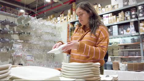 young woman choosing white plates in a store to buy.