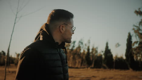 plano medio de un joven caucásico con gafas en la naturaleza disfrutando de una hermosa puesta de sol en la tarde