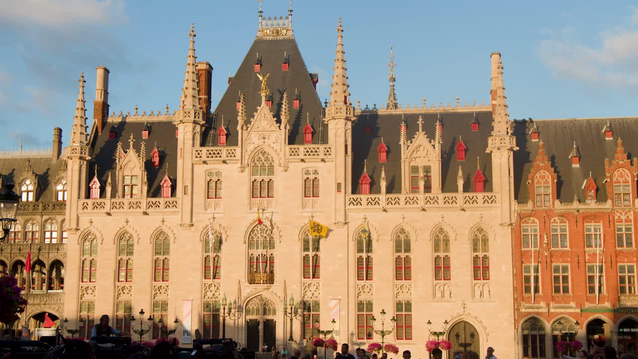 Static wide shot of Bruges city hall facade illuminated by warm evening sunlight, minimal movement