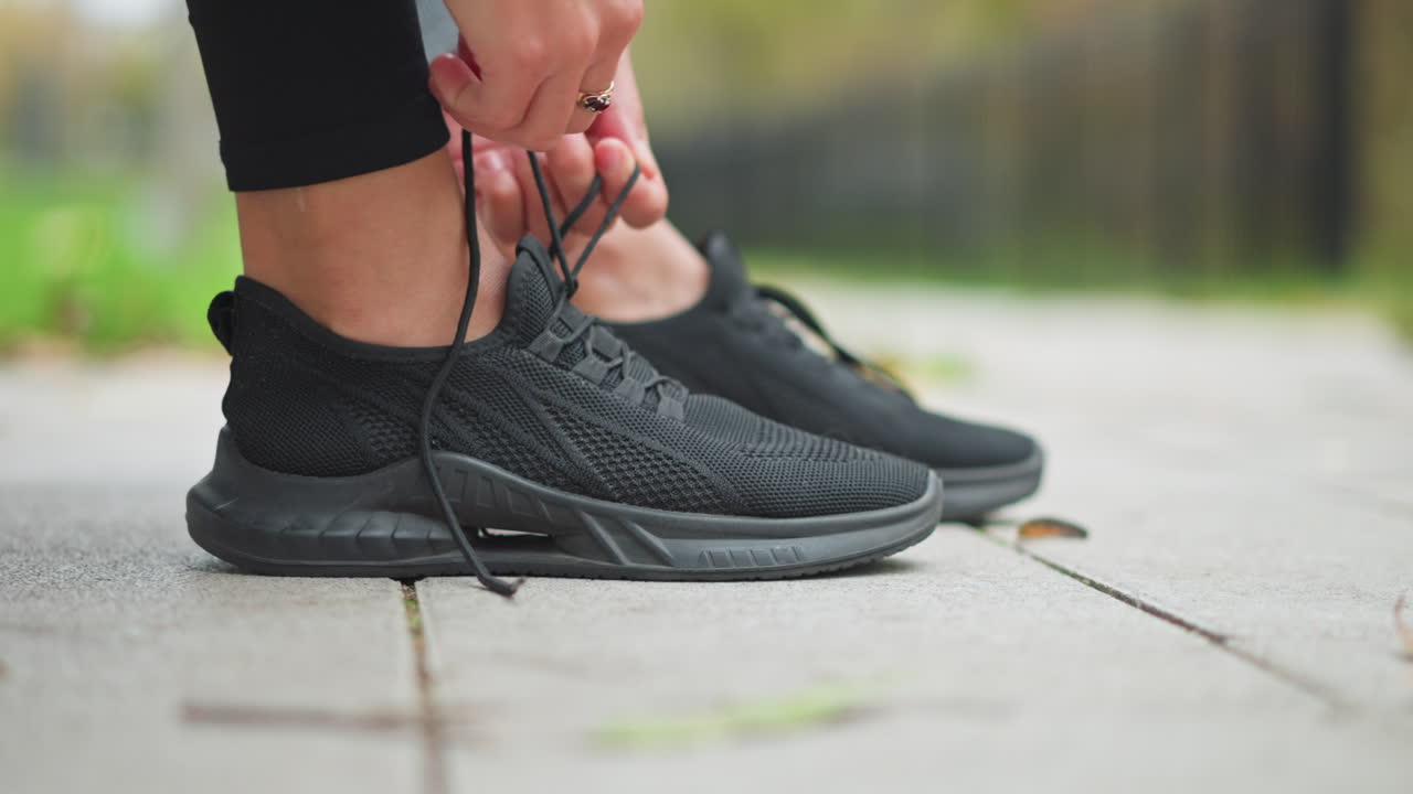 Close-up of lady tightening her black sneakers with golden ring on her finger, preparing for outdoor exercise or workout, focused on footwear and active lifestyle