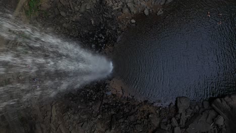 vista aérea de arriba hacia abajo de la piscina de la cascada y una mujer joven sentada en la roca en la parte superior