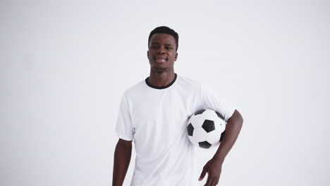 Portrait-of-a-happy-football-player-of-an-African-ethnic-group-in-a-white-uniform-on-a-white-background-with-a-ball-in-his-hands-Laughing-African-football-player