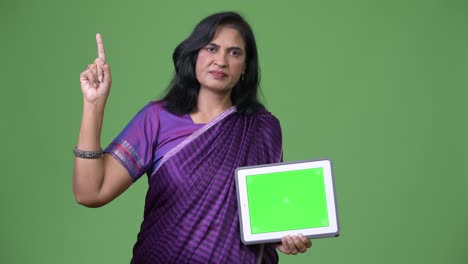 mature beautiful indian woman showing digital tablet and pointing finger up