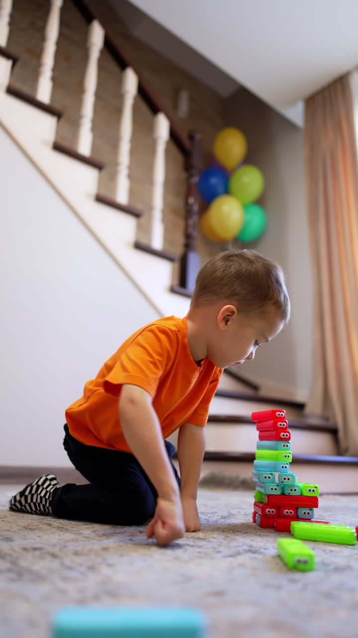 Caucasian kid sits on the floor playing with toys. Baby boy building a tower of blocks peacefully. Vertical video.