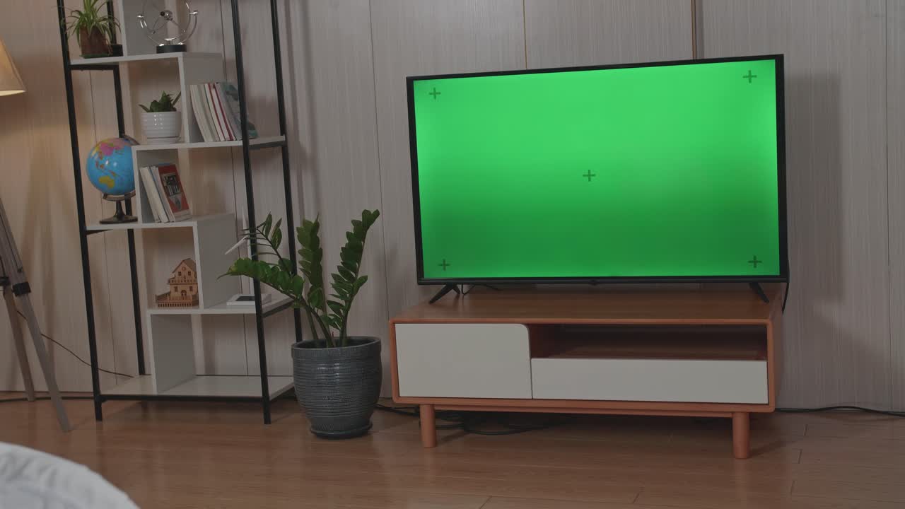 Man Holding Television Remote Control And Watches Green Mock-Up Screen Tv While Sitting On A Couch At Home In The Evening