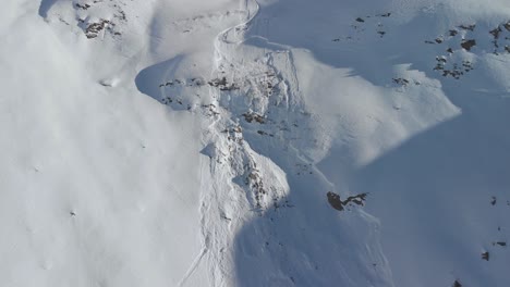 Aerial-view-away-from-a-small-avalanche-trail,-sunny,-winter-day,-in-Kaunertal,-Austria---pull-back,-drone-shot