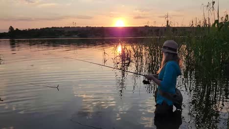 a woman fishing and wading in a tranquil lake with a stunning sunset in the background