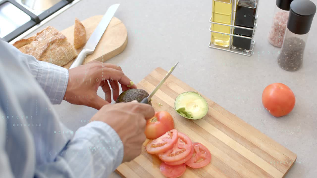 Man placing hands on avocado, using knife, slicing flesh beside tomato on cutting board for cooking