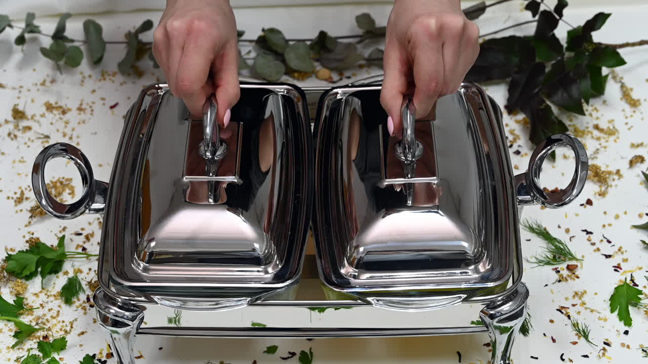 Close up of a woman taking off the lid of a chafing dish holding two separate trays filled with colorful dishes