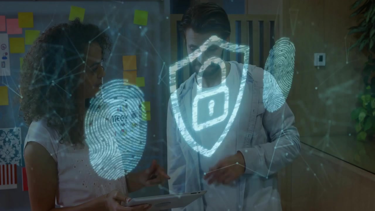 Two colleagues reviewing tablet in office, projecting hologram fingerprint scans and shield icon