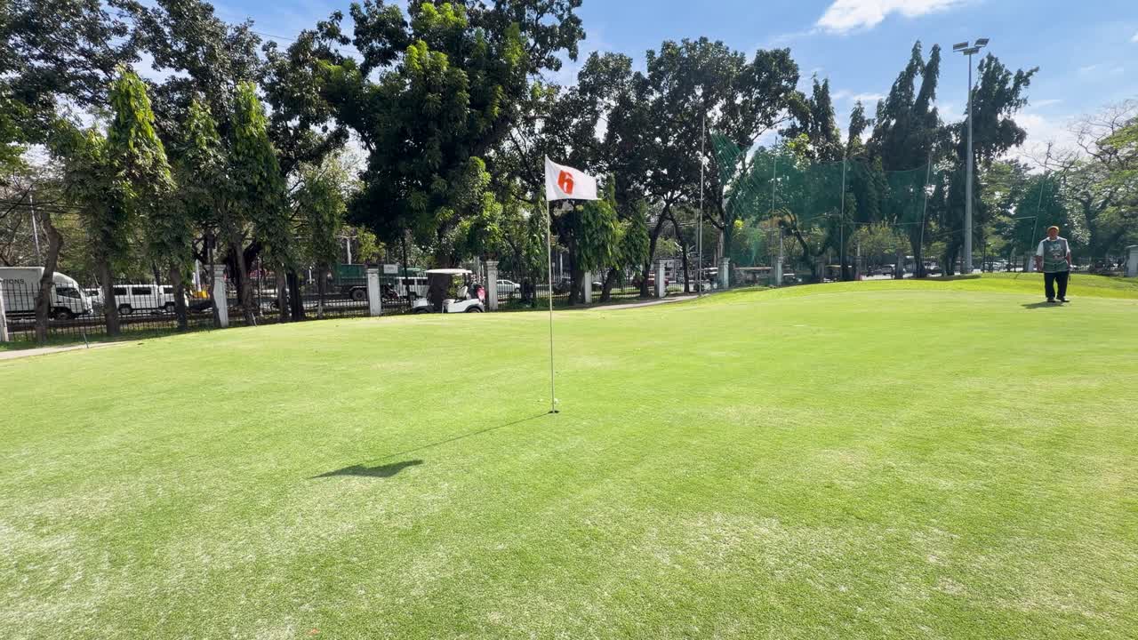 Inquadratura ampia di un golfista che imbuca su un green soleggiato mentre un caddy osserva.