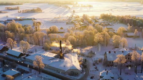 Small-township-with-industrial-buildings-and-smoking-chimneys,-aerial-view