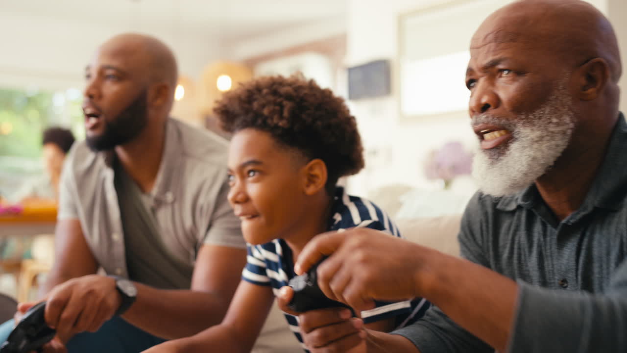 Multi-Generation Male Family Sitting On Sofa At Home Playing Video Game Together