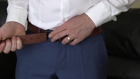 dressing up: man fastening belt over blue trousers and white shirt