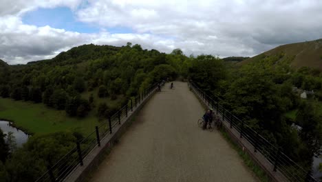 Aerial-view-of-cyclists-riding-over-the-Headstone-viaduct,-bridge-in-the-Derbyshire-Peak-District-National-Park,-Bakewell,-commonly-used-by-cyclists,-hikers,-popular-with-tourists-and-holiday-makers