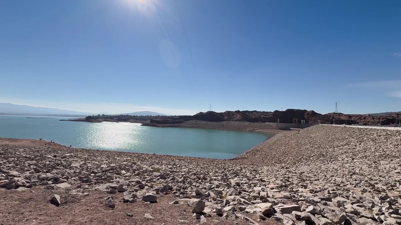 Il bacino idrico Dique Ullum riflette la luce solare intensa tra rive rocciose e creste montuose aride a Ullum, Provincia di San Juan, Cuyo, Argentina, inquadratura di apertura.