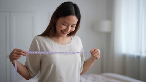 happy asian woman measuring herself with a tape