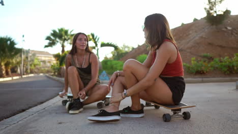 with the sun setting, two girls in a skate park relax on their boards, exchanging conversation, accompanied by smiles and hearty laughter. enjoying a longboard talk among friends