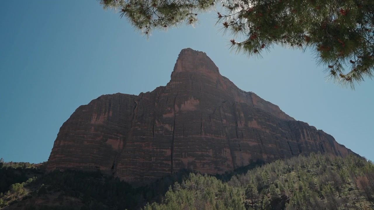 Imponente picco di roccia rossa della Cattedrale di Imsfrane che si erge sopra una pineta contro un cielo blu in Marocco.