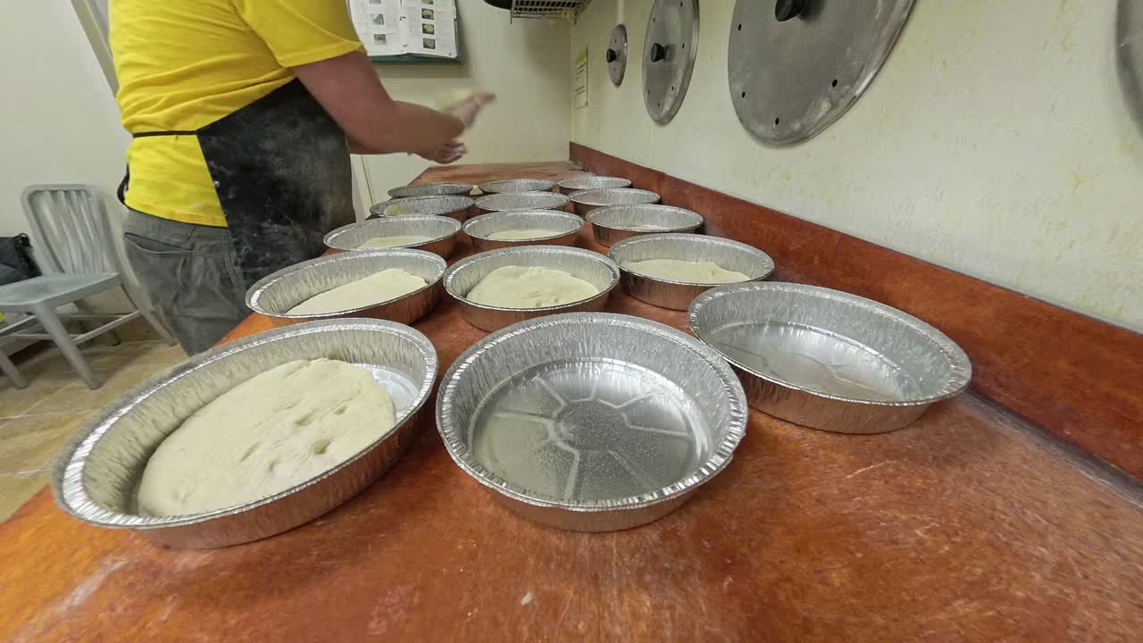 Arbeider plasserer rå pizzadeig i aluminiumsfoliebeholdere