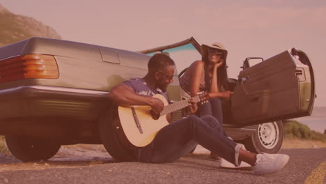 hombre afroamericano tocando la guitarra para su esposa cerca del coche en la calle