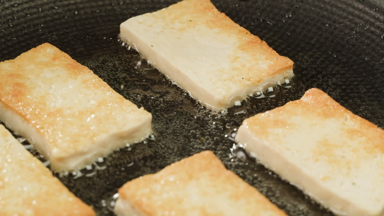 Fried tofu with sesame seeds and spices on cast iron pan, cooking japanese salad. Healthy ingredient for cooking vegan vegetarian diet food. Roasted tofu over black background.