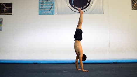 una foto fija de un tipo musculoso sin camisa haciendo el pino en el gimnasio de gimnasia