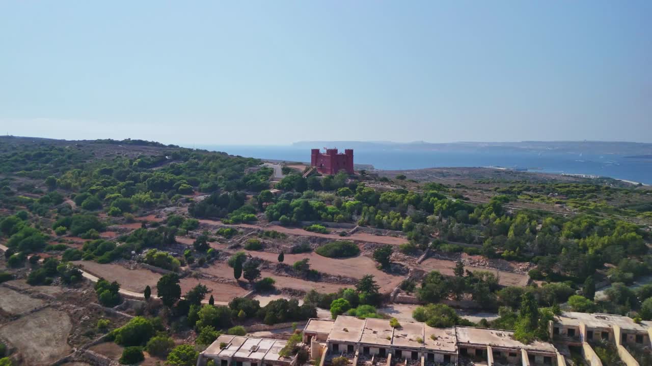 Aerial view of red castle, green landscape, and blue sea on a sunny day
