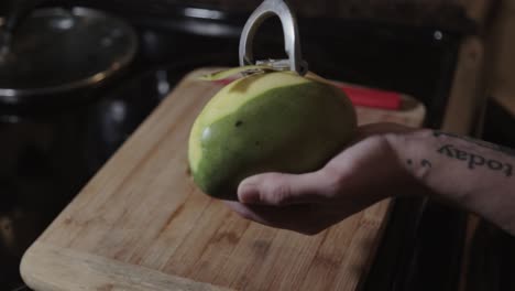 canadá - pelado de mango verde inmaduro con un pelador sobre la tabla de cortar de madera - toma de primer plano