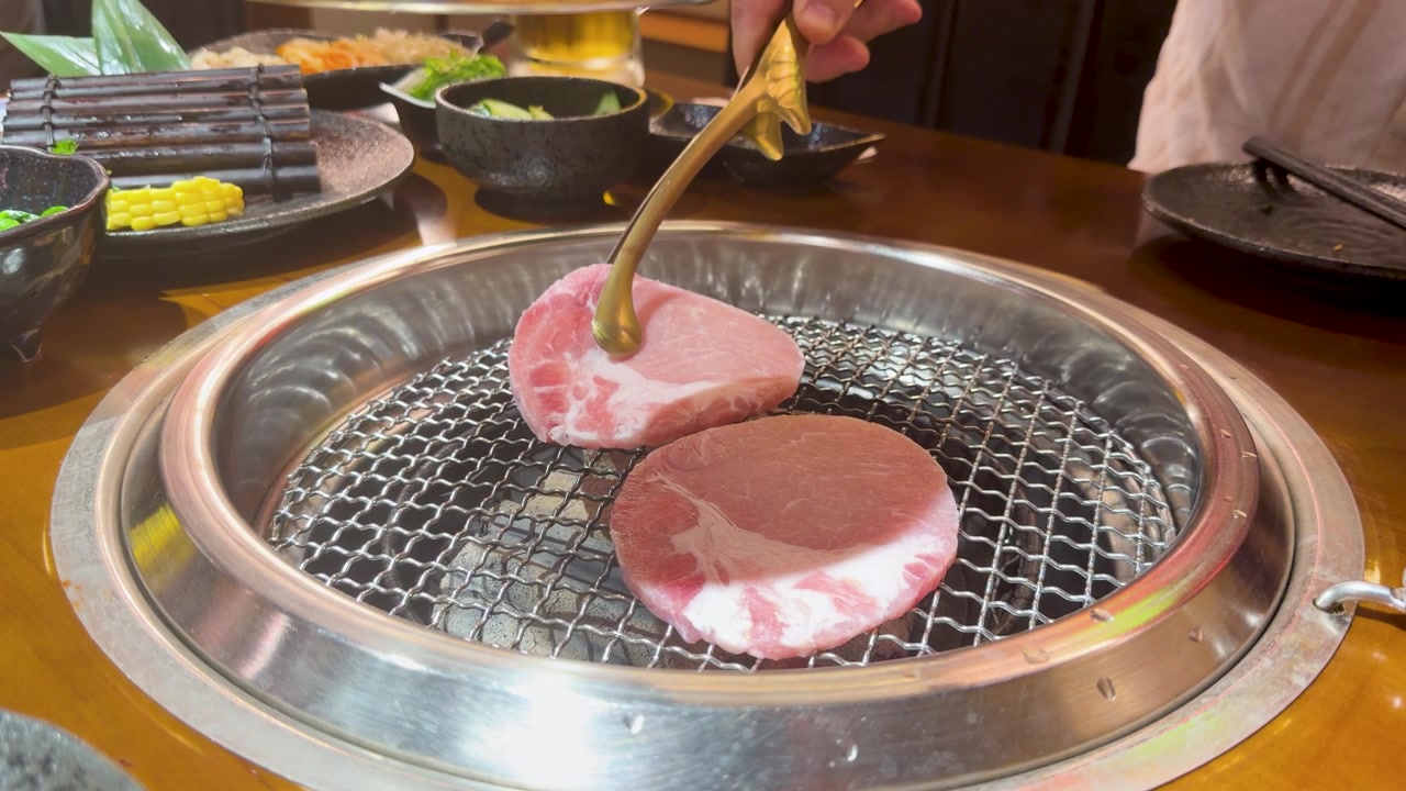 Metalltang plasserer rå svinekjøttskiver på en varm kullgrill på en asiatisk restaurant.