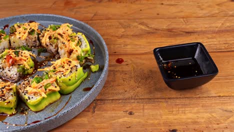 primer plano de las manos con palillos, tomando un rollo de sushi de aguacate y sumergiéndolo en salsa de anguila