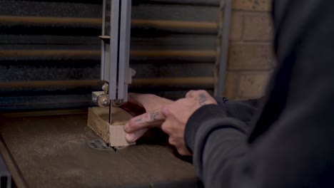 slow motion close-up of man with tattoos cutting hardwood block with electric bandsaw machinery blade tool for indoor climbing holds in diy home garage shed australia carpentry industry building craft