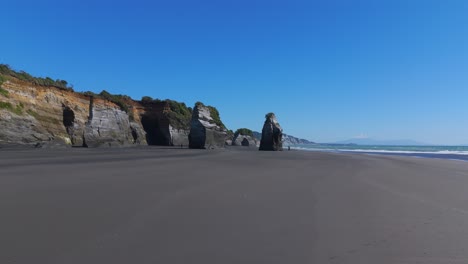 Flying-over-the-black-volcanic-sand-beach-of-tree-sisters-and-elephant-rock