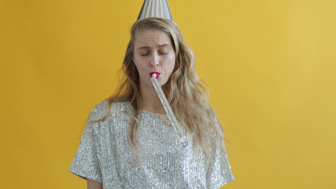 Woman blowing a party horn, looking unhappy