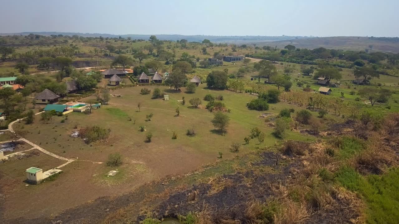 Drone footage captures a safari lodge complex on the riverbank of the Nile in Uganda, surrounded by open grassland, acacia trees and scattered bush
