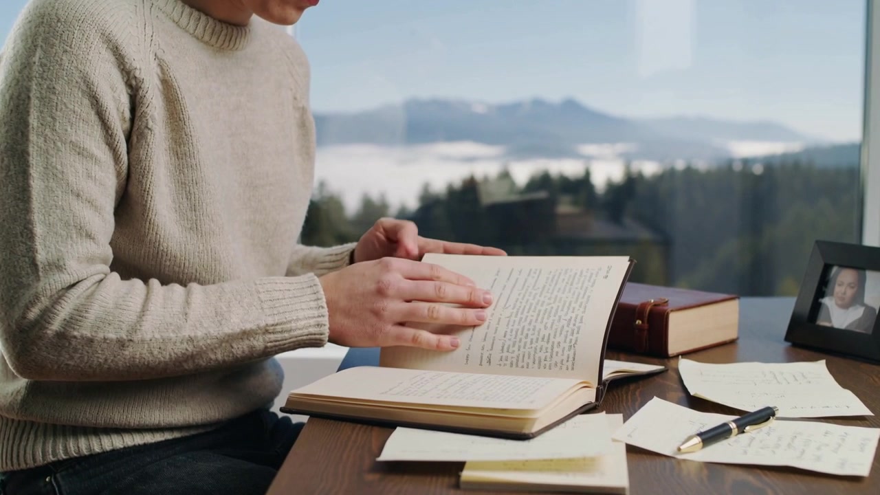 Placing hand on notebook, writer in beige knit sweater flipping pages reviewing notes at desk