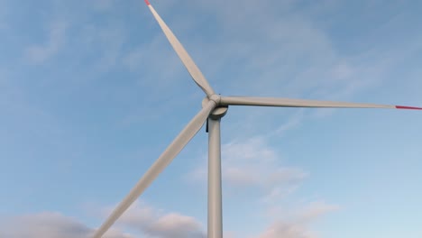 Sleek wind turbine stands tall against a clear sky, its blades spinning gracefully in the breeze. The surrounding landscape features rolling green fields, symbolizing clean and renewable energy.