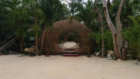 Aerial-view-towards-a-wooden-structure-with-a-circular-opening-for-decoration,-weddings-and-events,-surrounded-by-tropical-and-palm-trees