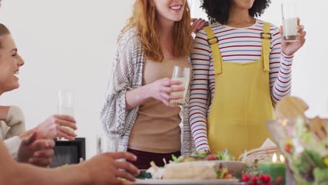 Happy-group-of-diverse-friends-sitting-at-table-and-eating-dinner-together,-making-toast