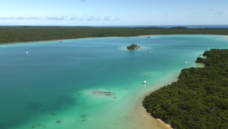 Traditional-pirogue-boats-with-sails-transport-tourists-in-Upi-Bay,-Isle-of-Pines---aerial