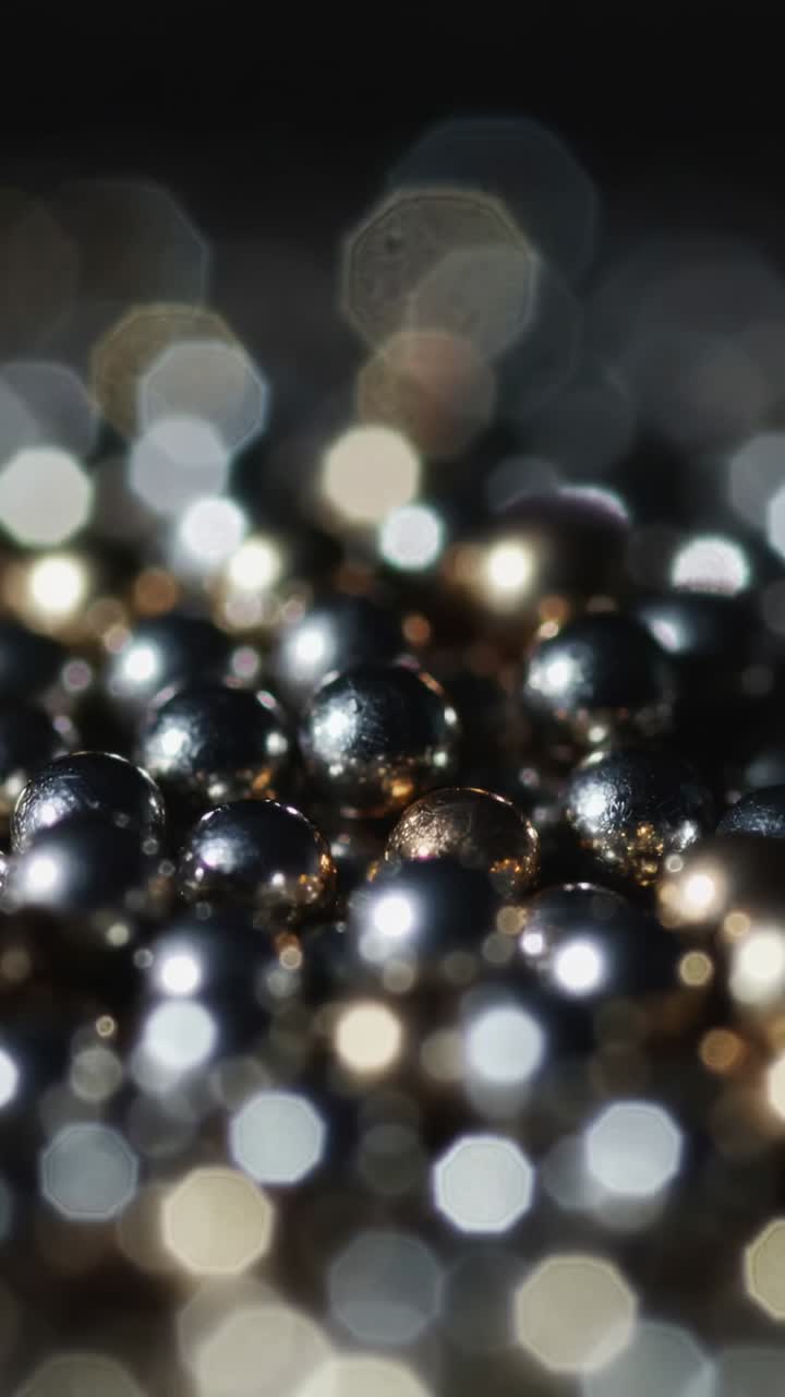 Video verticale: cambio di messa a fuoco e illuminazione che rivela delle perle metalliche in studio, creando un effetto bokeh esagonale
