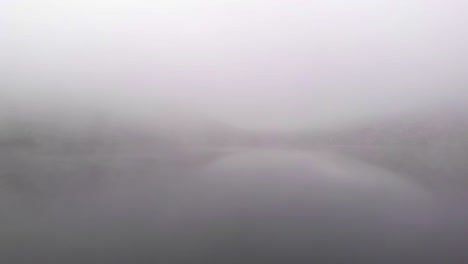 Mann-Steht-Auf-Einem-Felsen,-Neblige-Seenlandschaft,-Drohnenaufnahme