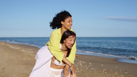 Two women enjoying a piggyback ride on the beach