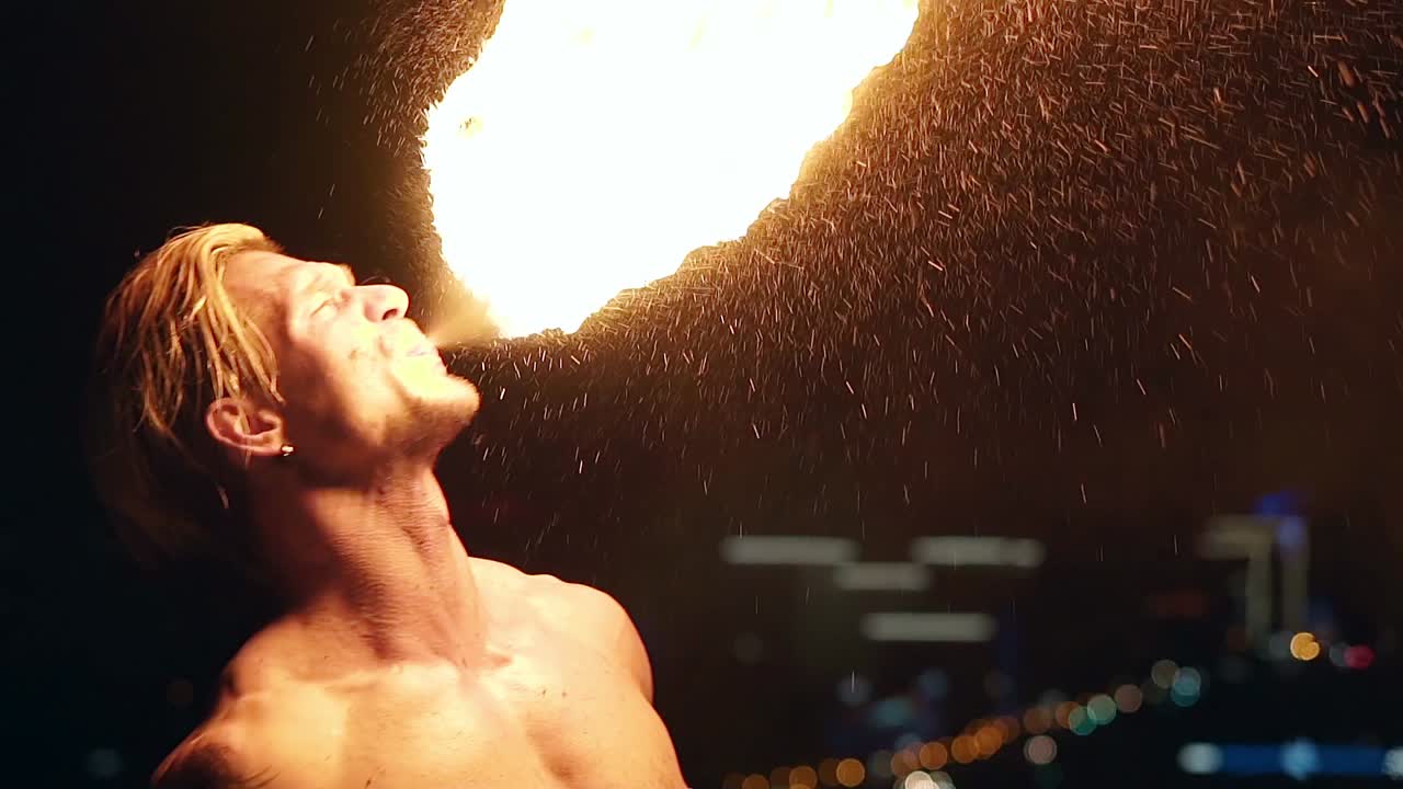 젊은 금발 남성이 큰 불의 흐름을 어내며 불공을 만들고 느린 속도 클로즈업