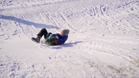 boy sledding down the hill in winter. cute boy with saucer sled riding from snowy slide outdoors. slow motion.