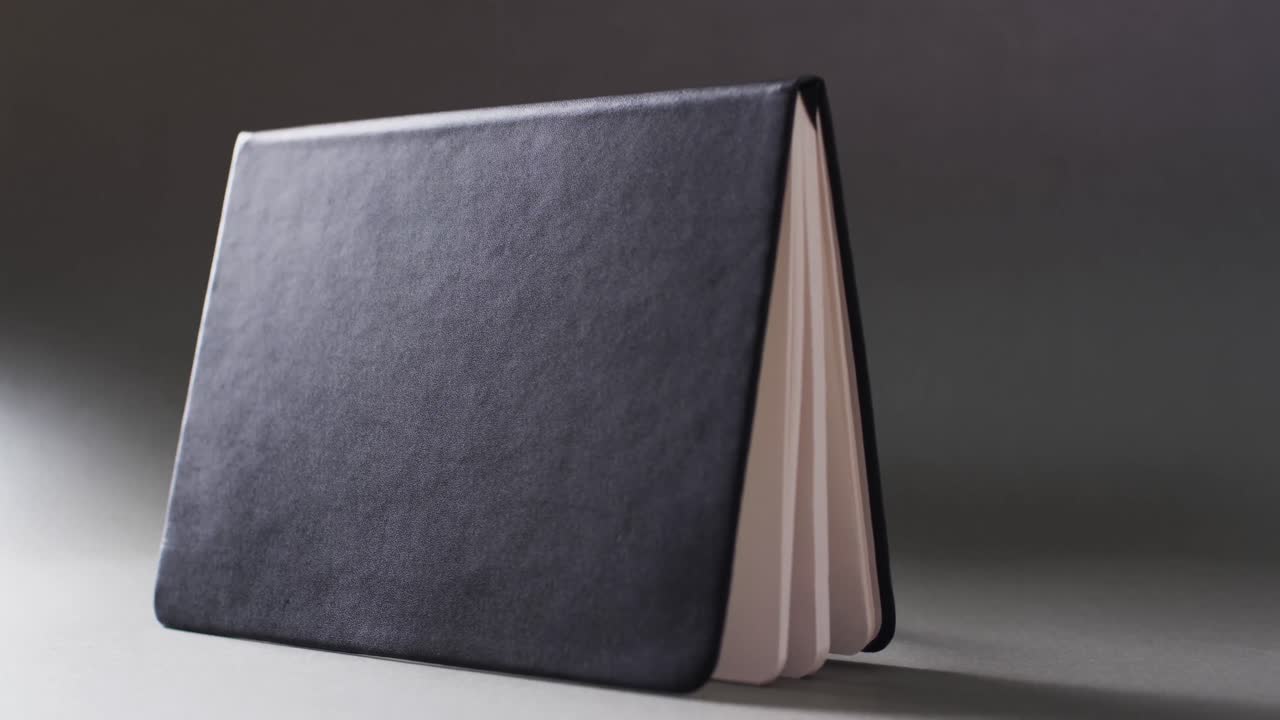 Close up of open black book standing horizontal with copy space on gray background in slow motion