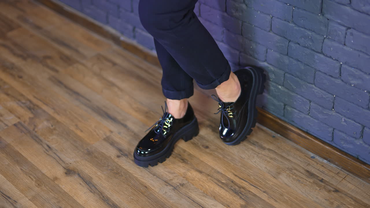 Demonstration of fashionable black shoes on tractor soles with laces. Model in jeans and shoes stands at the blue brick wall.