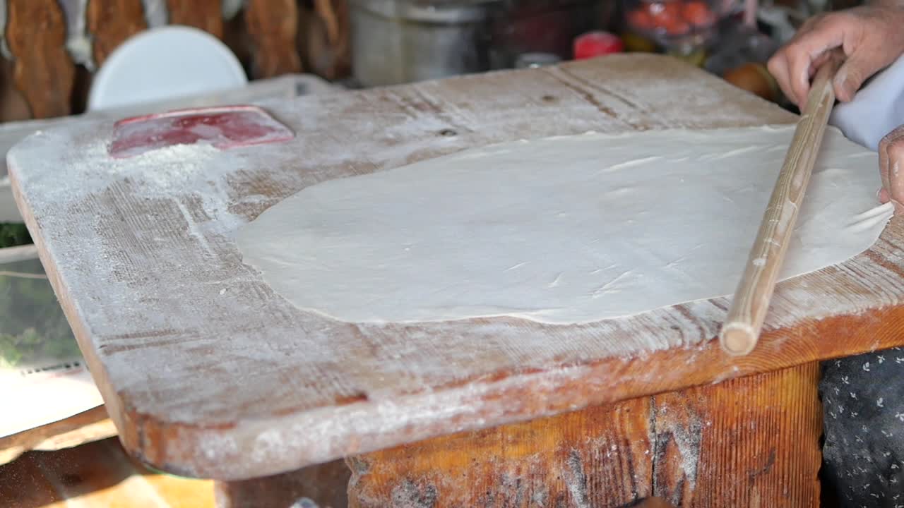 Mani che tirano una sfoglia sottile su tagliere di legno infarinato